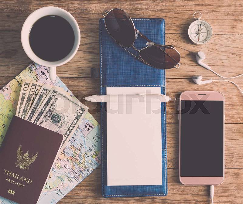 Notebook, Pen, Sunglasses, Coffee Cup, Passport, Money, Mobile Phone, Earphones, Map and Compass on wooden plank. Travel Concept, stock photo