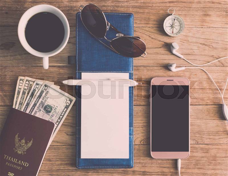 Notebook, Pen, Sunglasses, Coffee Cup, Passport, Money, Mobile Phone, Earphones and Compass on wooden plank. Travel Concept, stock photo