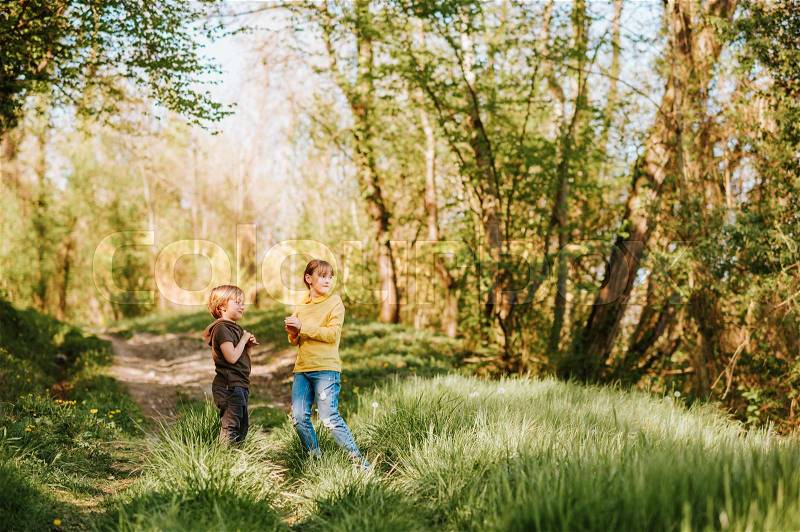Two funny kids playing together in spring forest, little brother and sister enjoying nice walk in woods, stock photo