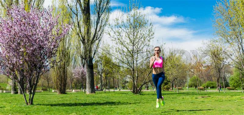 Woman running for better fitness though a sunny park in spring, stock photo