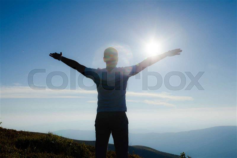 Silhouette of a person with hands up raised during the sunset on the top of the mountain, stock photo
