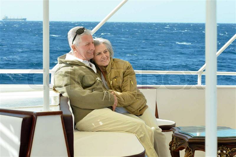 Smiling elderly couple resting on yacht in sea, stock photo