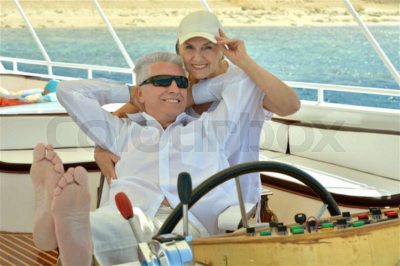 Smiling elderly couple resting on yacht in sea, stock photo