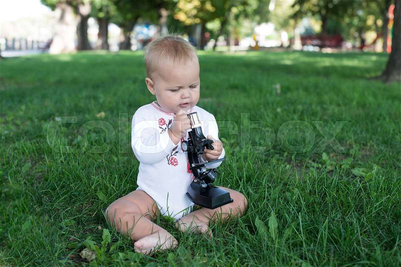 Student little girl with microscope - working outside in nature, stock photo