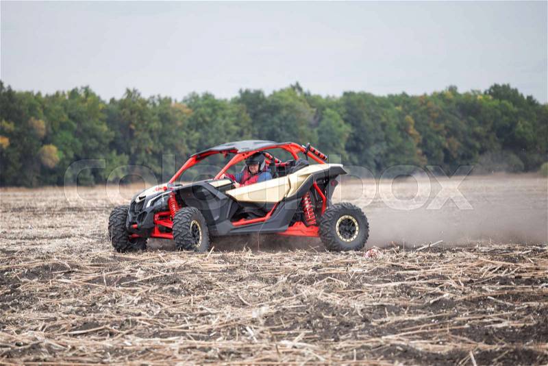 Driver at the wheel of quad bike is riding around the field in the dust. The concept of freedom and speed, stock photo