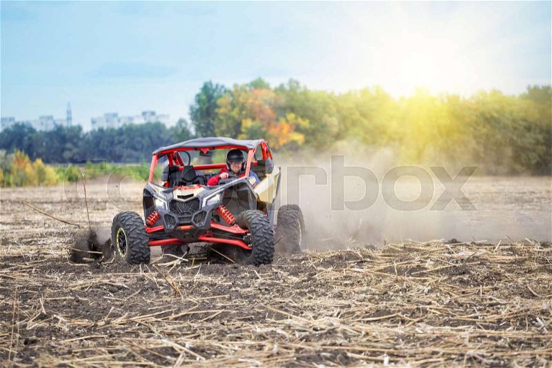 Man at the wheel of quad bike is riding around the field in the dust. The concept of freedom and speed, stock photo