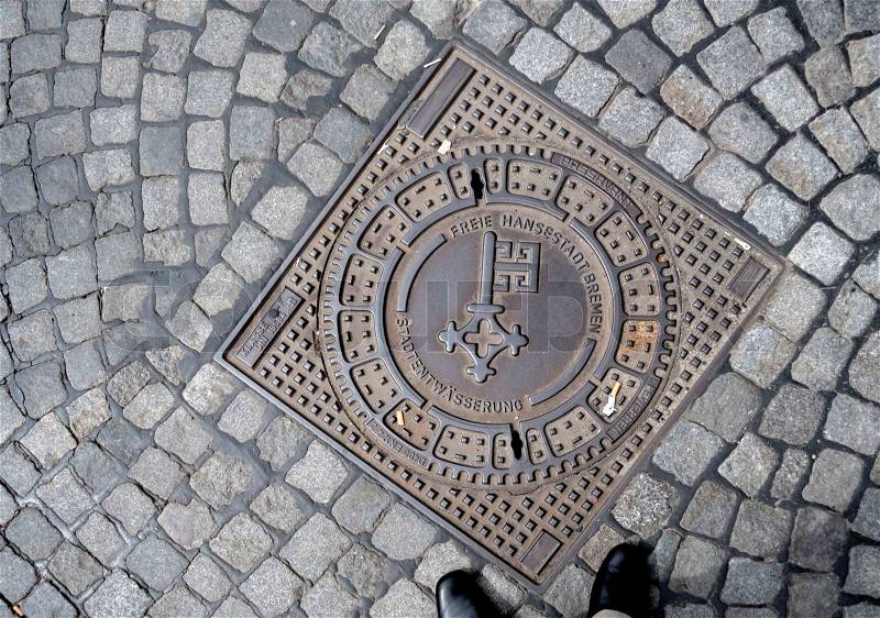Man standing in front of a water cover in street Bremen city logo in it, stock photo