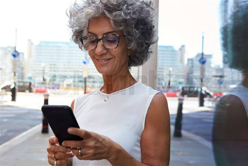 Middle aged woman using smartphone in city street, close up, stock photo