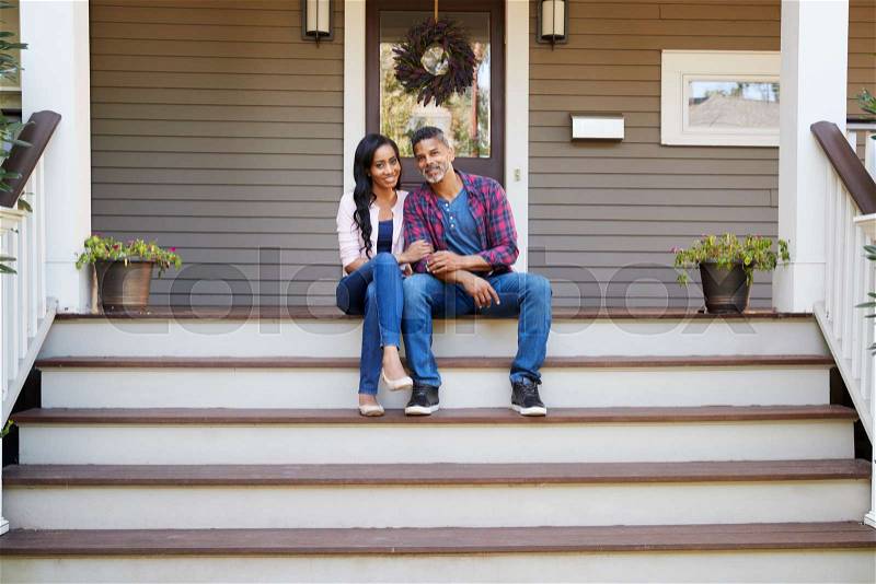 Couple Sitting On Steps Leading Up To Porch Of Home, stock photo