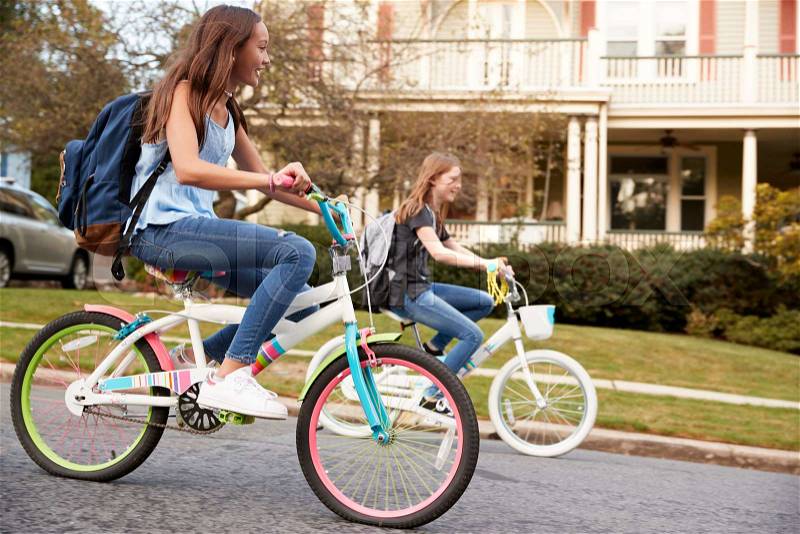Two teen girls riding bikes in street, side view close up, stock photo
