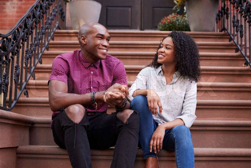 Couple Sit And Talk On Stoop Of Brownstone In New York City, stock photo