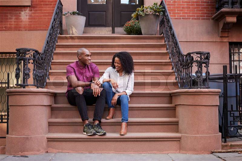 Couple Sit And Talk On Stoop Of Brownstone In New York City, stock photo