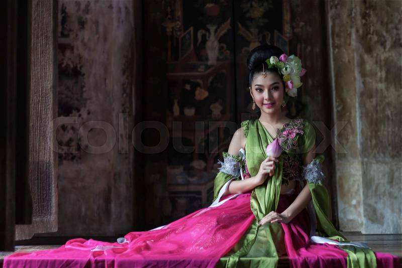 Beautiful Thai woman wearing a national costume and holding a lotus sitting beside a window.Lifestyle and culture of the ancient woman, Thailand, stock photo