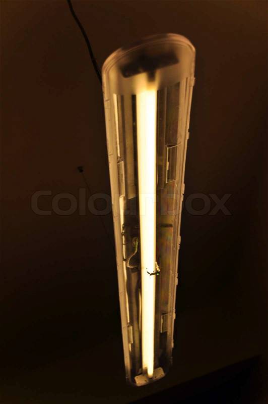 A fluorescent light mounted on the ceiling, emitting yellow light, stock photo