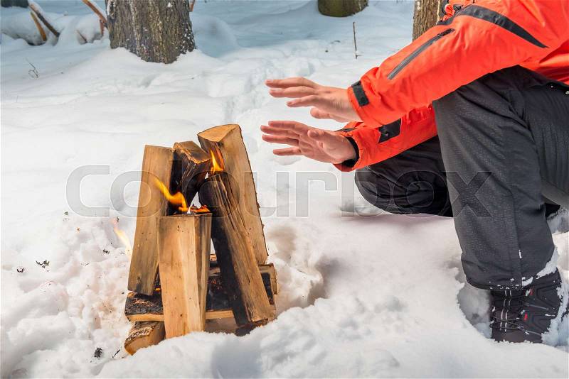 A bonfire in the winter forest and a tourist heating his hands by the fire, stock photo