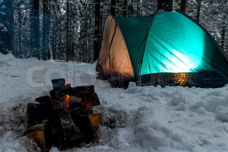 Focus on the fire in the snow against the background of the green tent in the winter forest, stock photo