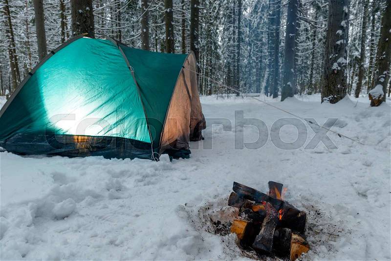 Light inside the tent in the winter forest, a nearby fire is burning, there are no people, stock photo