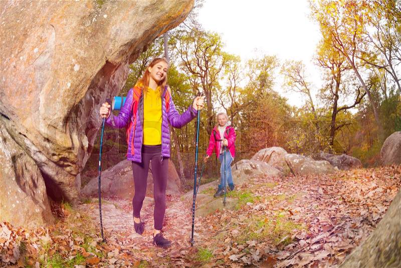 Happy tourists, young woman and girl with trekking sticks exploring mountain trails in autumn, stock photo
