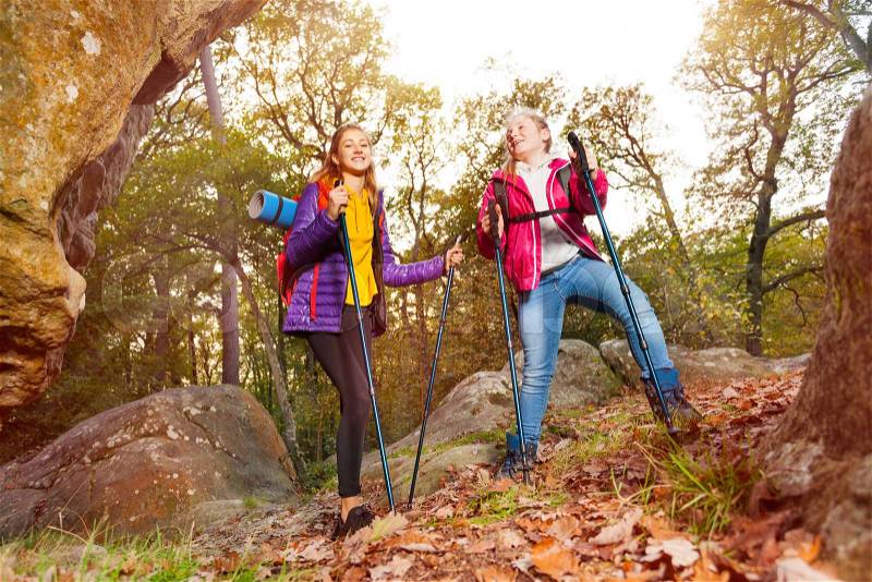 Happy travelers, young woman and teenage girl with backpacks walk along a trail towards a mountain in autumn, stock photo