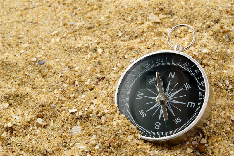 Compass on the sea-sand with patches of light on glass, stock photo
