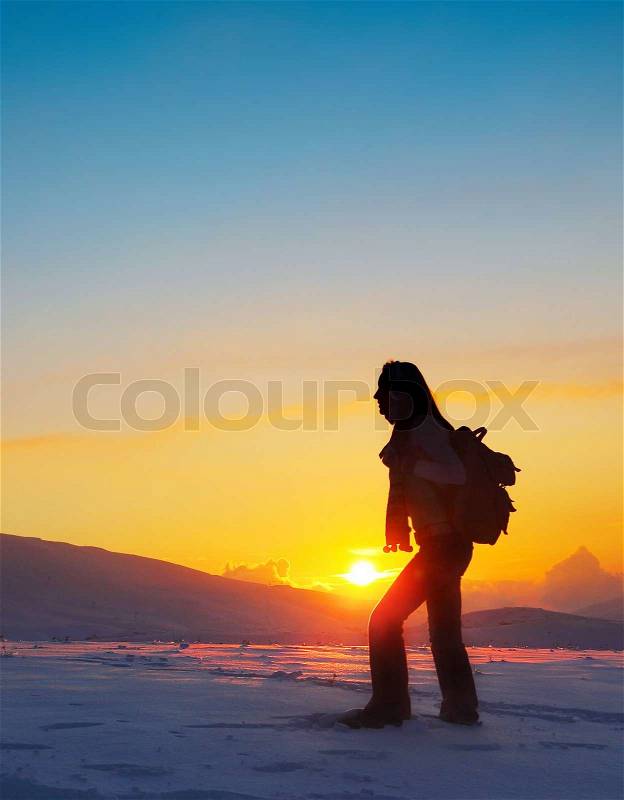 Woman traveler hiking in winter mountains, trekking in wintertime cold snowy weather, girl silhouette over natural colorful sky with bright sunset and beautiful landscape, freedom concept, stock photo