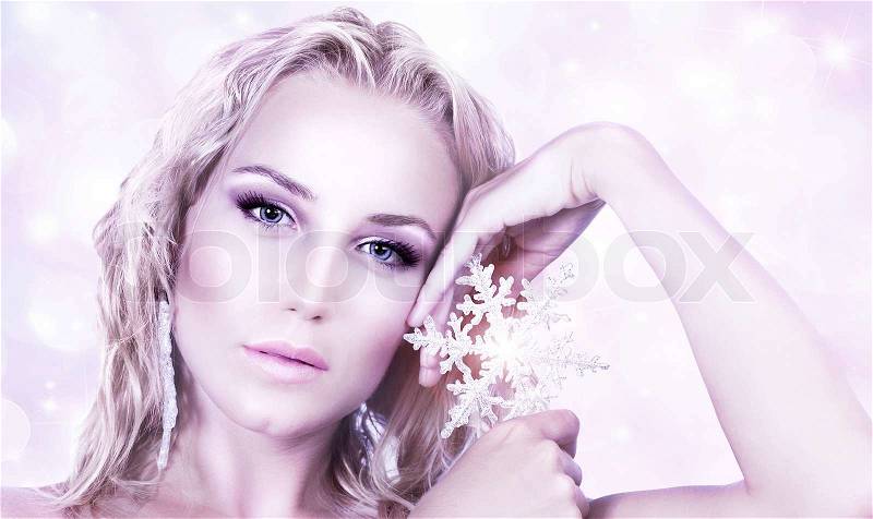Beautiful woman in Christmas winter style, holding shining snowflake star, glamor female face with bright makeup, sexy girl portrait over abstract pink glowing bokeh holiday background, stock photo