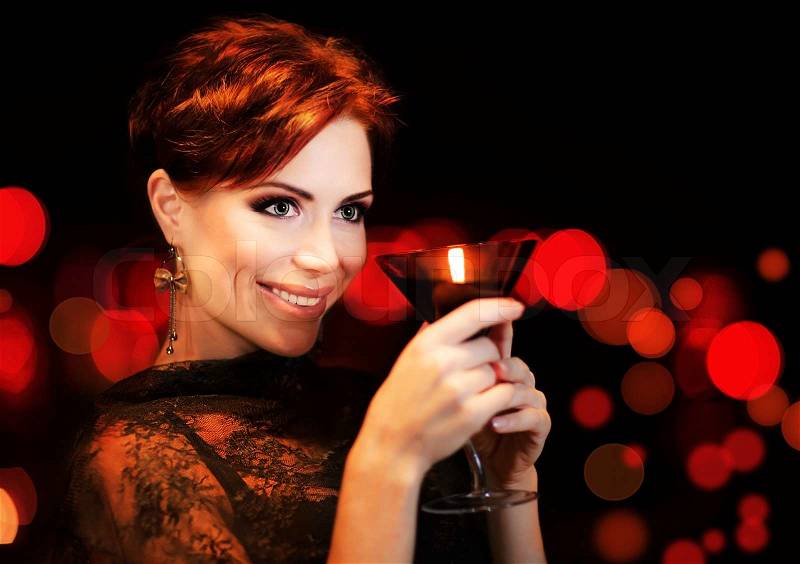 Beautiful female partying, celebrating holiday, portrait of a woman holding martini glass, girl over black background with red blur bokeh lights, luxury nightlife, stock photo
