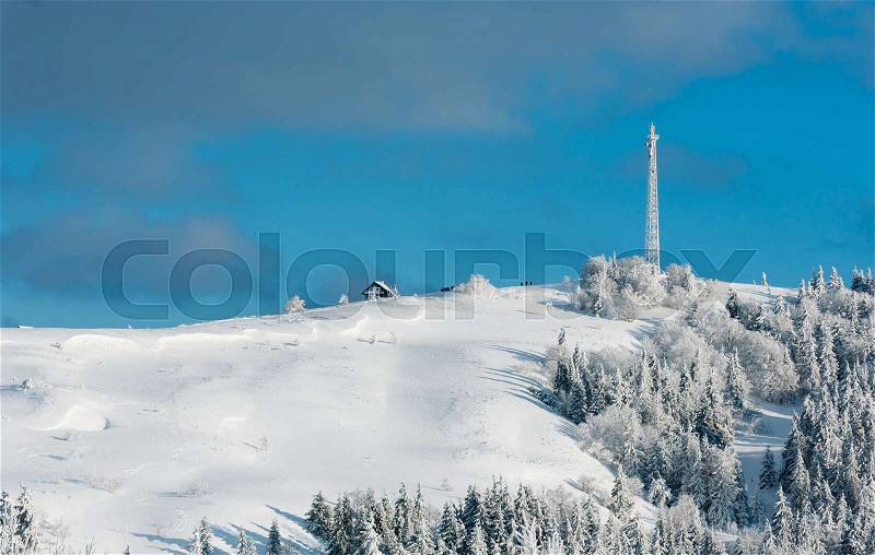 Beautiful winter rime frosting trees, communication tower and snowdrifts on mountain top on blue cloudy sky background (Carpathian mountain, Ukraine). People are unrecognizable, stock photo