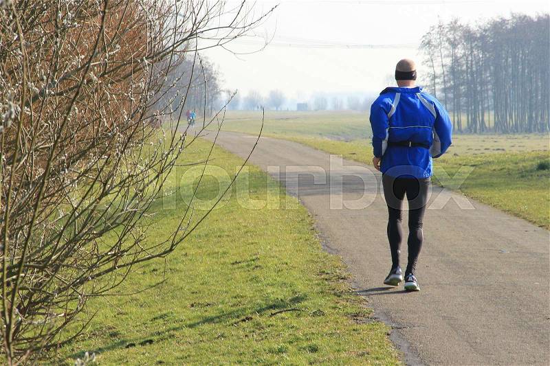 The male runner is training for the marathon and is running along blooming catkins in the park on a sunny day in spring, stock photo