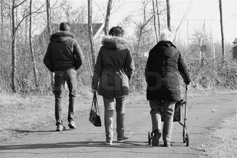 The retired mom with her rollator is walking with her daughter and son-in-law in the park on a sunny day in the mild winter in black and white, stock photo