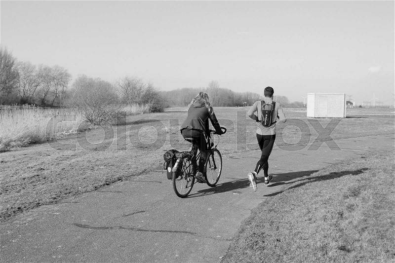 The girl is biking and her boyfriend with a black rucksack is training for the marathon at the countryside in the soft winter in black and white, stock photo