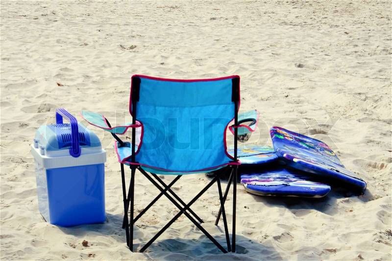 A blue nylon chair, cooler, and surf boards on a sandy beach, stock photo