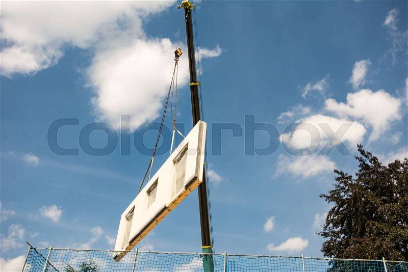 Assembling a prefabricated house - wall is hanging on a crane, stock photo