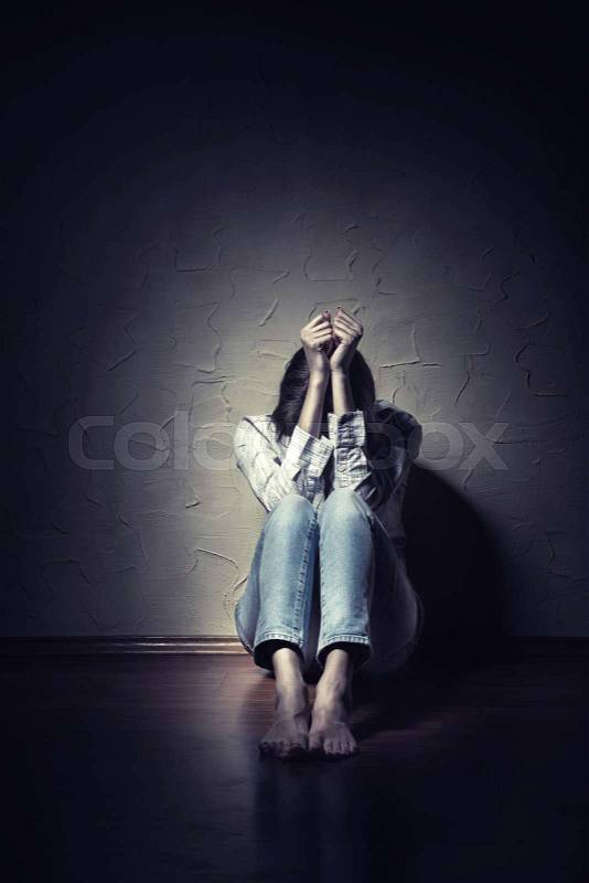 Young sad woman sitting alone on the floor in an empty room, stock photo