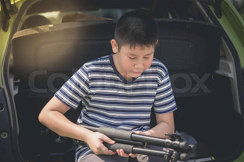 Asian boy sitting in rear door car and holding tripod, lifestyle concept, stock photo