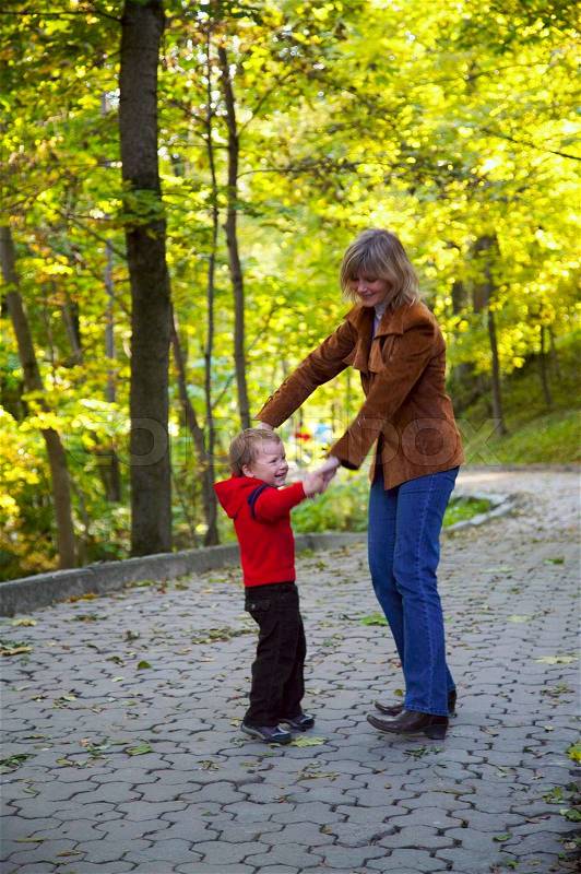 Happy family mother with small boy funny dance in golden autumn city park, stock photo