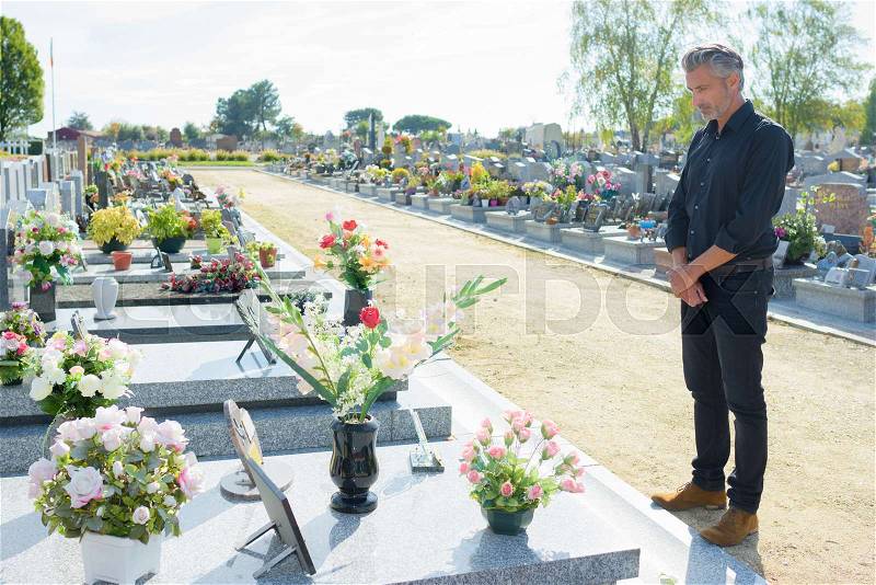 Man stood alone looking at grave, stock photo