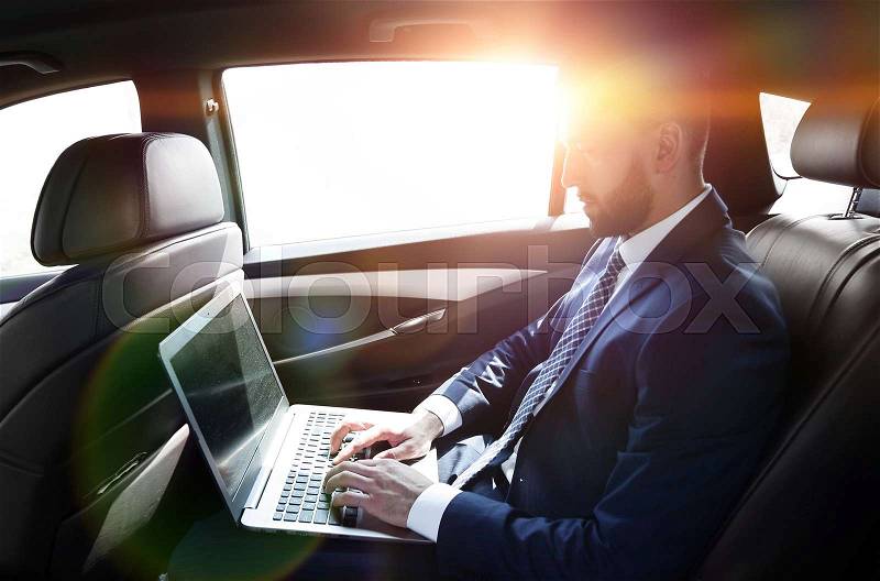 Side view of a businessman using a laptop in the backseat of a car, stock photo