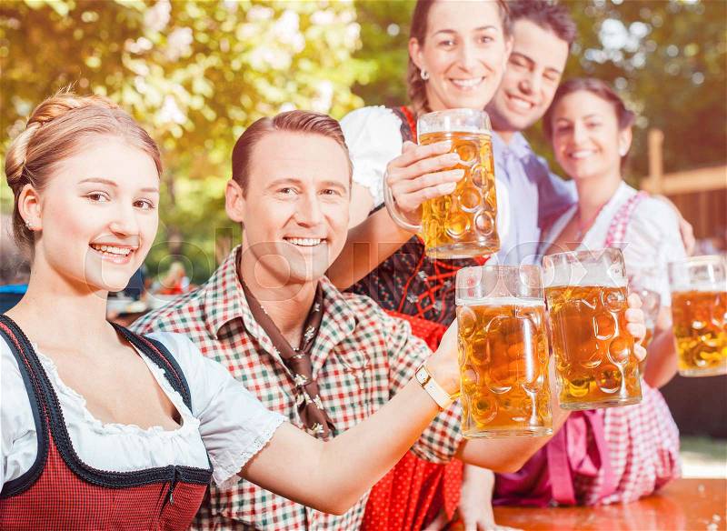 In Beer garden - friends in Tracht, Dirndl and Lederhosen drinking a fresh beer in Bavaria, Germany, stock photo