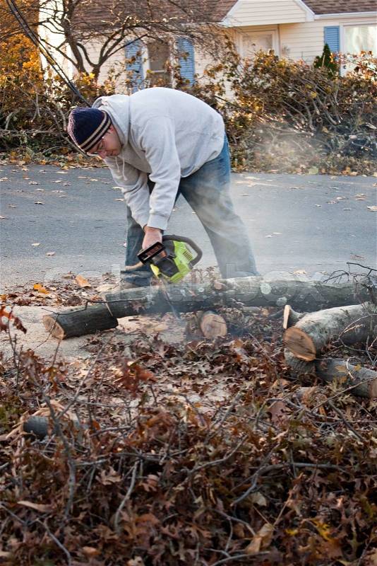Man cutting tree limbs with a chainsaw that have fallen from storm damageA late fall snow storm in the month of October was the cause, stock photo