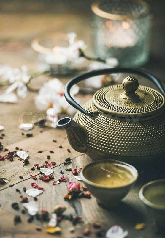 Traditional Asian tea ceremony arrangement. Iron teapot, cups, blooming almond flowers, dried rose buds and candles over wooden table background, selective focus, stock photo