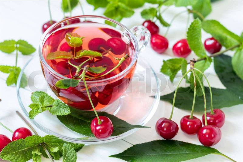 Fresh fruit cherry drink in transparent glass cup surrounded by cherries on the white wooden background. Top view, stock photo