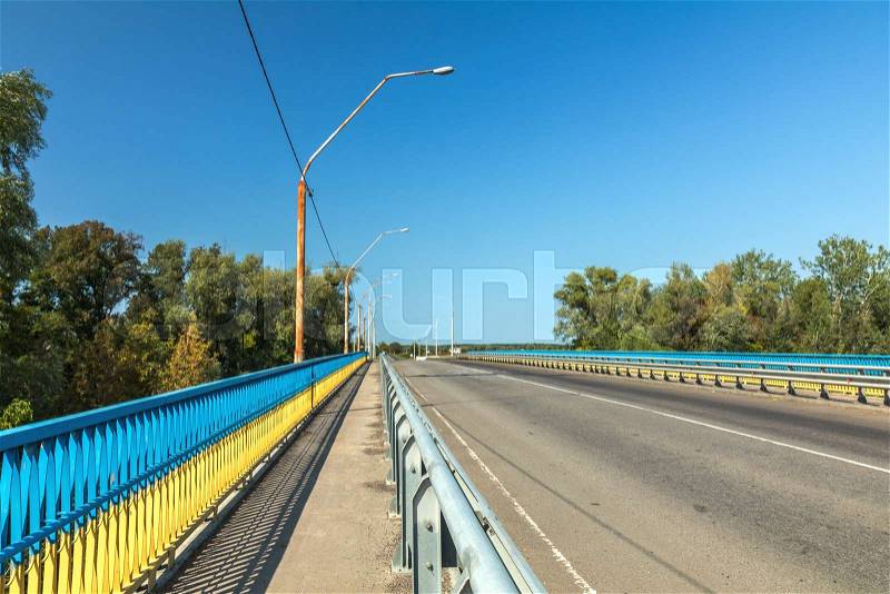 Bridge over river with street lights. Summer sunny beautiful day on outside city highway. Barrier decorate with Ukraine national colors, stock photo