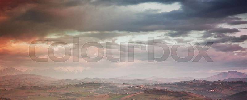 Italian rural landscape. Province of Fermo, Italy. Villages and fields on hills under colorful cloudy sky, stock photo