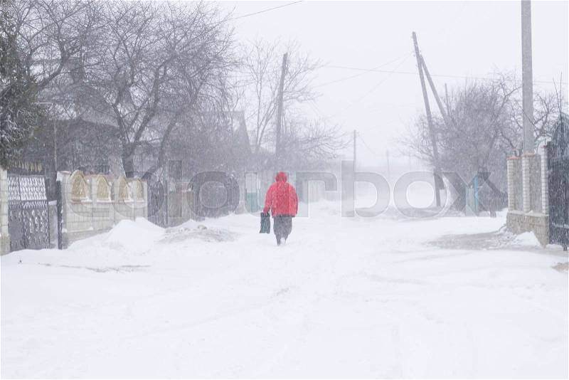 A snowy village street during a snow storm and a man in a red jacket, stock photo