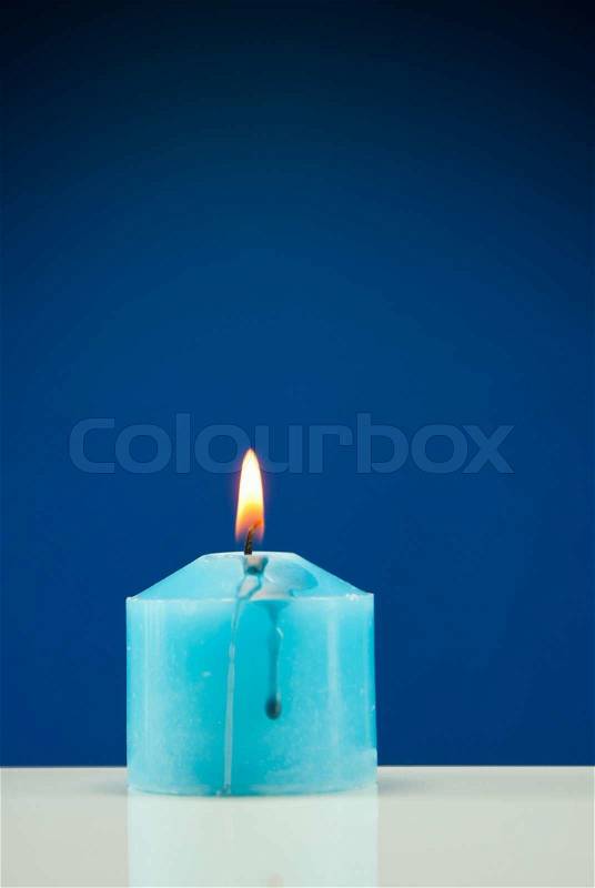 Close up of burning candle against dark blue background, stock photo