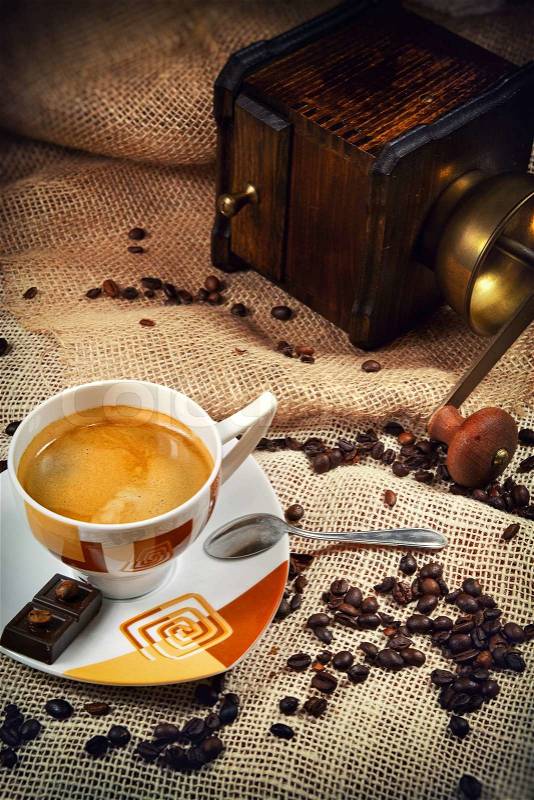 Coffee cup surrounded by coffee grains and coffee-mill in background, stock photo
