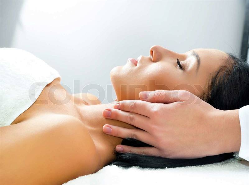 Beautiful young woman receiving facial massage with closed eyes in a spa center, stock photo