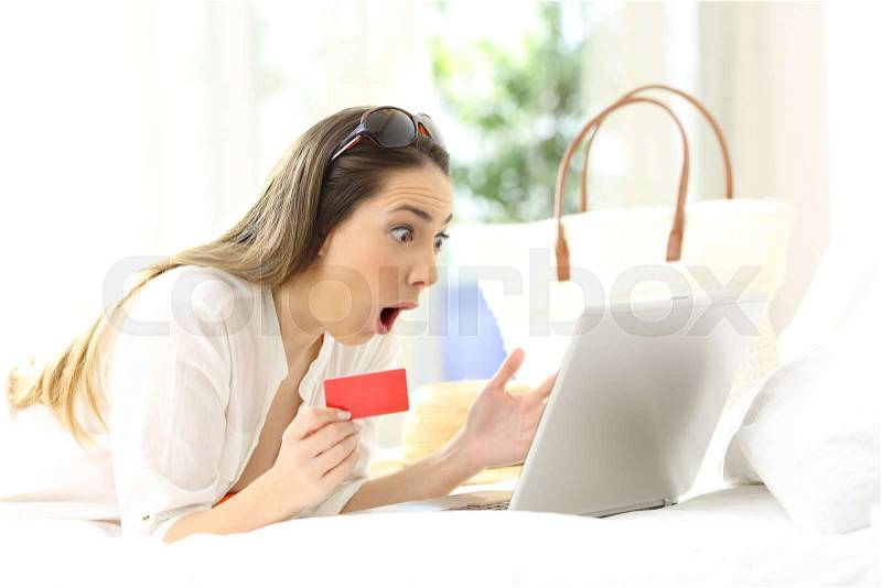 Amazed woman buying on line lying on a bed in an hotel rrom in summer vacations, stock photo