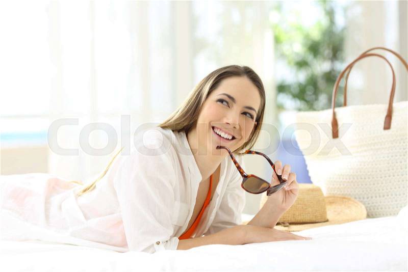 Hotel guest wondering looking above lying on a bed of a room on summer vacations, stock photo